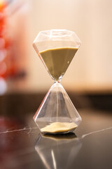 A sandglass or hourglass is placed on table. Interior decoration object photo, selective focus.