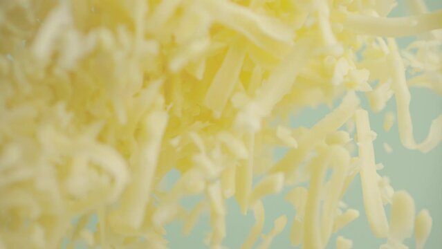 Heap grated cheddar cheese flying in slow motion close up. Shredded yellow parmesan cheese falling in macro