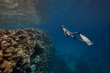 Freediver woman swim in blue ocean over coral reef