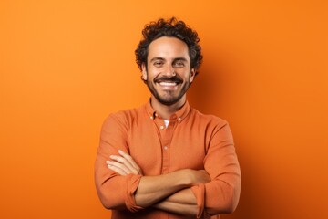 Portrait of a joyful man in his 30s with arms crossed over soft orange background