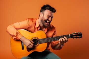 Portrait of a grinning man in his 30s playing the guitar over soft orange background