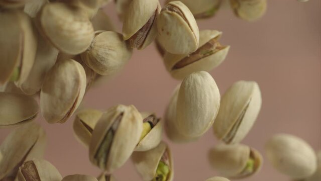 Flying in air fresh raw whole and cracked pistachios on brown background. Pistachio nuts are falling in slow motion. Concept organic diet