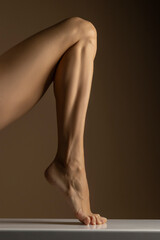 closeup, side view of female foot and leg posing on beige background