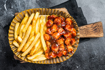 German currywurst with french fry served in a steel plate. Black background. Top view