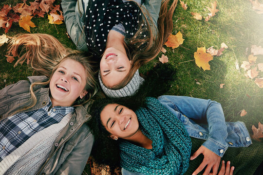 Above, teenagers or girls on park for autumn, relaxing and bonding together on grass with happiness. Nature, lawn and friends on summer holiday for chilling, hanging out and laugh outdoors with smile