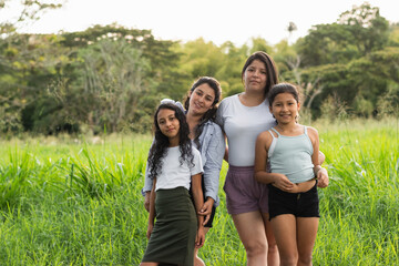 two young Latin women posing with their daughters in the middle of a field on a summer day