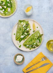 Green pancakes with spinach and nettles, stuffed with asparagus, green peas and ricotta on a ceramic plate on a gray concrete background. Seasonal products, recipes. Asparagus recipes.