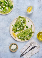 Green pancakes with spinach and nettles, stuffed with asparagus, green peas and ricotta on a ceramic plate on a gray concrete background. Seasonal products, recipes. Asparagus recipes.