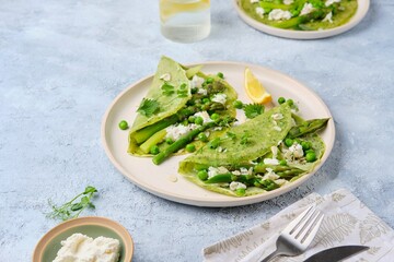 Green pancakes with spinach and nettles, stuffed with asparagus, green peas and ricotta on a ceramic plate on a gray concrete background. Seasonal products, recipes. Asparagus recipes.