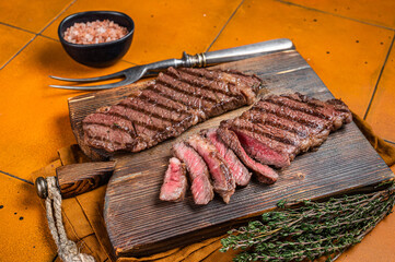 BBQ grilled denver top blade beef meat steak with thyme on a wooden board. Orange background. Top...