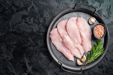 Raw sliced chicken breast fillet steaks in a steel tray, fowl meat. Black background. Top view....