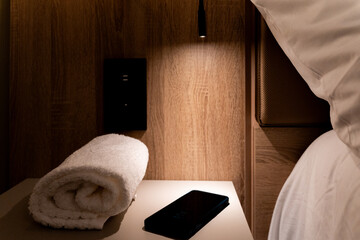 Room side table next to the bed illuminated by small lamp with mobile and towel