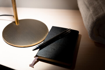 Close up of leather diary with pen on top and lamp base illuminating hotel room table