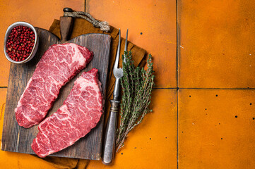 Raw Denver beef meat Steak with pink pepper and thyme. Orange background. Top view. Copy space