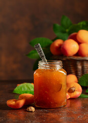 Apricot jam in glass jar and fresh fruits on a brown table.