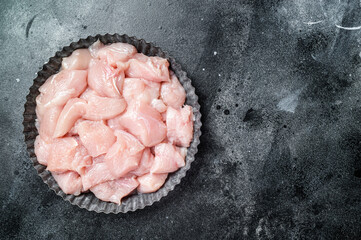 Diced raw chicken breast fillets on a plate, poultry meat. Black background. Top view. Copy space