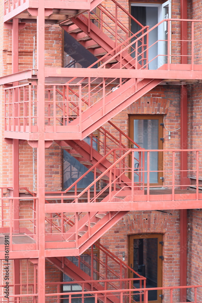 Poster a red fire escape staircase next to a brick building. suitable for urban architecture concepts