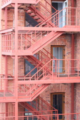A red fire escape staircase next to a brick building. Suitable for urban architecture concepts