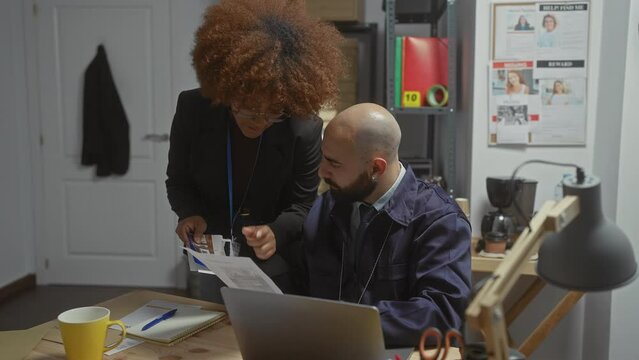 A woman and a man analyze documents in a detective's office with posters, laptops, and coffee cups indicating an investigative workspace.