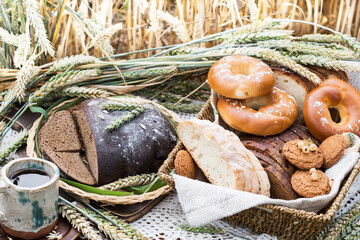 Sliced rye bread, other pastries in wicker tray and mug with bread drink kvass on lace tablecloth with wheat ears in wheat field background