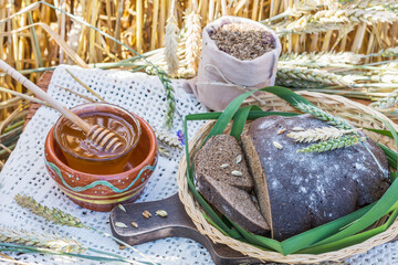 Sliced rye bread, fresh honey and bag of cumin on lace tablecloth with wheat ears in wheat field...