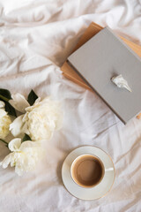 An inviting scene of a warm coffee cup and lush peonies on a bed, capturing the vibe of a relaxed morning. The soft natural light, tranquility atmosphere. Morning in bed aesthetic concept.