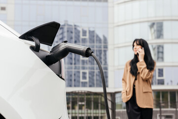 Close-up female hands unplug charger plug from charging station to his electric car before driving around city center. Eco friendly rechargeable car powered by sustainable and clean energy