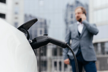 Businessman plugging electric car from charging station. Senior is plugging in power cord to an electric car. Charging electric car at charging station.