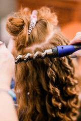 A woman with red hair is getting her hair curled with a heating wand. 