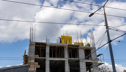 A building under construction with yellow formwork and scaffolding, featuring concrete slabs and...