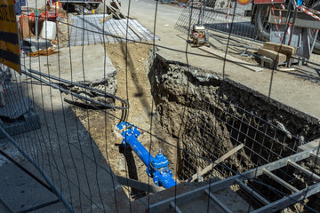 An open trench on a construction site with blue pipe, metal fence, and concrete reinforcement,...