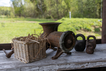 A rustic scene featuring a weathered meat grinder, metal weights, and a wicker basket on a wooden...