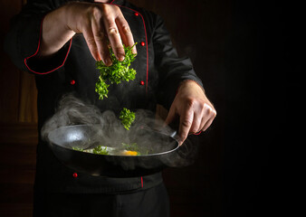 Cooking scrambled eggs with parsley in a frying pan. The cook hand throws fresh parsley into the...