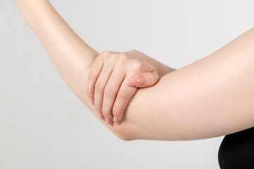 Close-up view of caucasian woman rubbing her elbow using hand against grey background. Soft focus. Healthcare, cosmetics and self massage theme.	