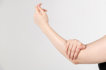 Close-up view of caucasian woman rubbing her elbow using hand against grey background. Soft focus....
