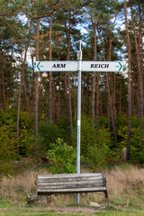 ARM und REICH - Wegweiser hinter einer alten Sitzbank - deutsch
