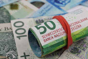 A roll of Swiss franc banknotes shown against the flat Polish zloty banknotes, CHF, PLN
