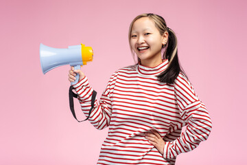 Happy cute Asian girl posing in studio holding megaphone, looking at camera, isolated
