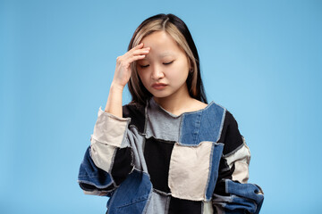 Portrait of Asian girl posing in studio having a headache, isolated on blue