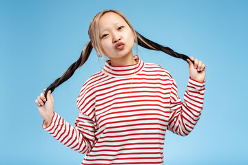 Pretty Asian girl holding her ponytails while making air kiss by lips looking at camera, isolated