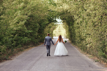 Rear view of bride and groom in wedding clothes holding their hands and  walking along the tunnel...