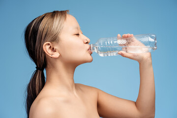 Pretty Asian girl posing with closed eyes drinking water holding bottle, isolated on blue