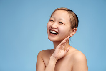 Happy Asian girl with bare shoulders laughing looking at camera, touching her face by hand