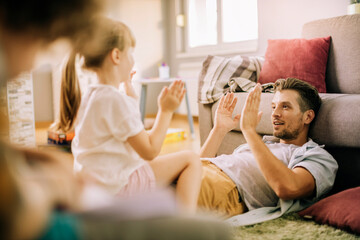 Father playing with daughter at home and clapping hands