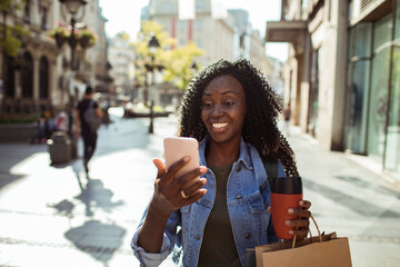 African American woman checking smartphone while shopping in city
