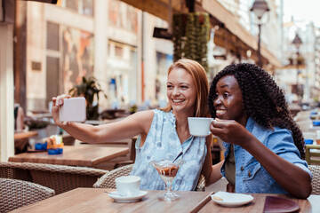 Two young women taking selfie in street cafe