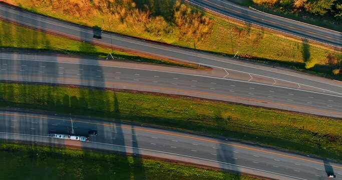 Highways divided by the green grass. Cars go quickly by the roads. Top view on the motorway at sunset.