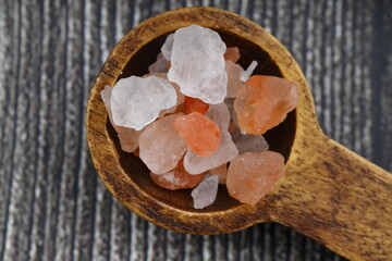 Pink Himalayan salt is poured with a wooden spoon. Himalaya salt on a dark background. Copy space....