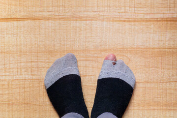 feet wearing torn stockings with the big toe sticking out of a hole,on a wooden background,concept of need or comfort at home