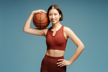 Beautiful asian woman playing basketball, holding ball looking at camera isolated